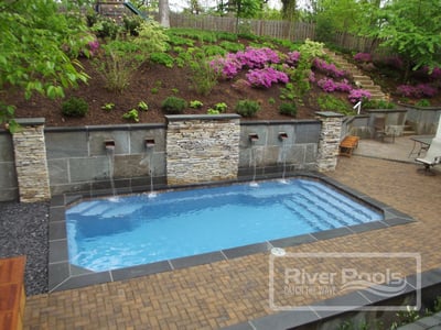 retaining wall with water features behind rectangular fiberglass pool