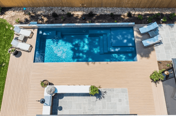 Aerial view of modern rectangular fiberglass inground pool with tanning ledge and composite deck patio.
