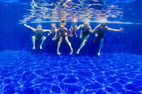 Underwater view of a smiling family holding hands and swimming together in a clear blue pool, capturing a joyful moment of connection and fun during a summer swim.