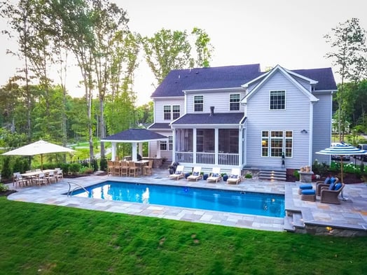 Backyard with a blue pool, mowed grass, landscaping and a house.