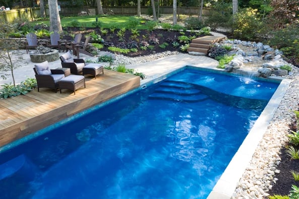 Blue rectangular pool with sun shelf surrounded by landscaping