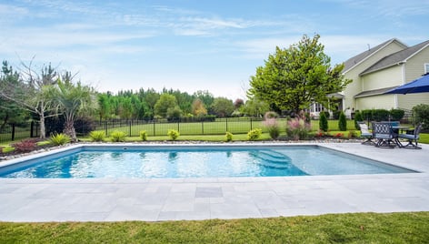 Fiberglass pool installed by River Pools Charlotte, featuring a rectangular design, light gray paver patio, and black aluminum fencing in a landscaped backyard.