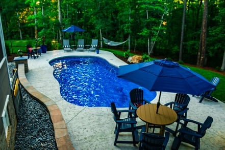 Blue, freeform pool design with an umbrella and landscaping around it.