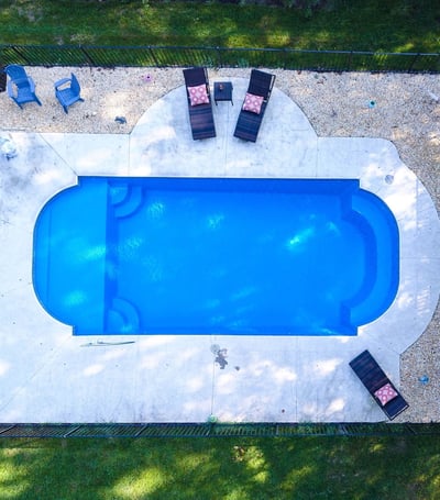 Attractive inground fiberglass pool with a simple poured concrete deck with furniture. 