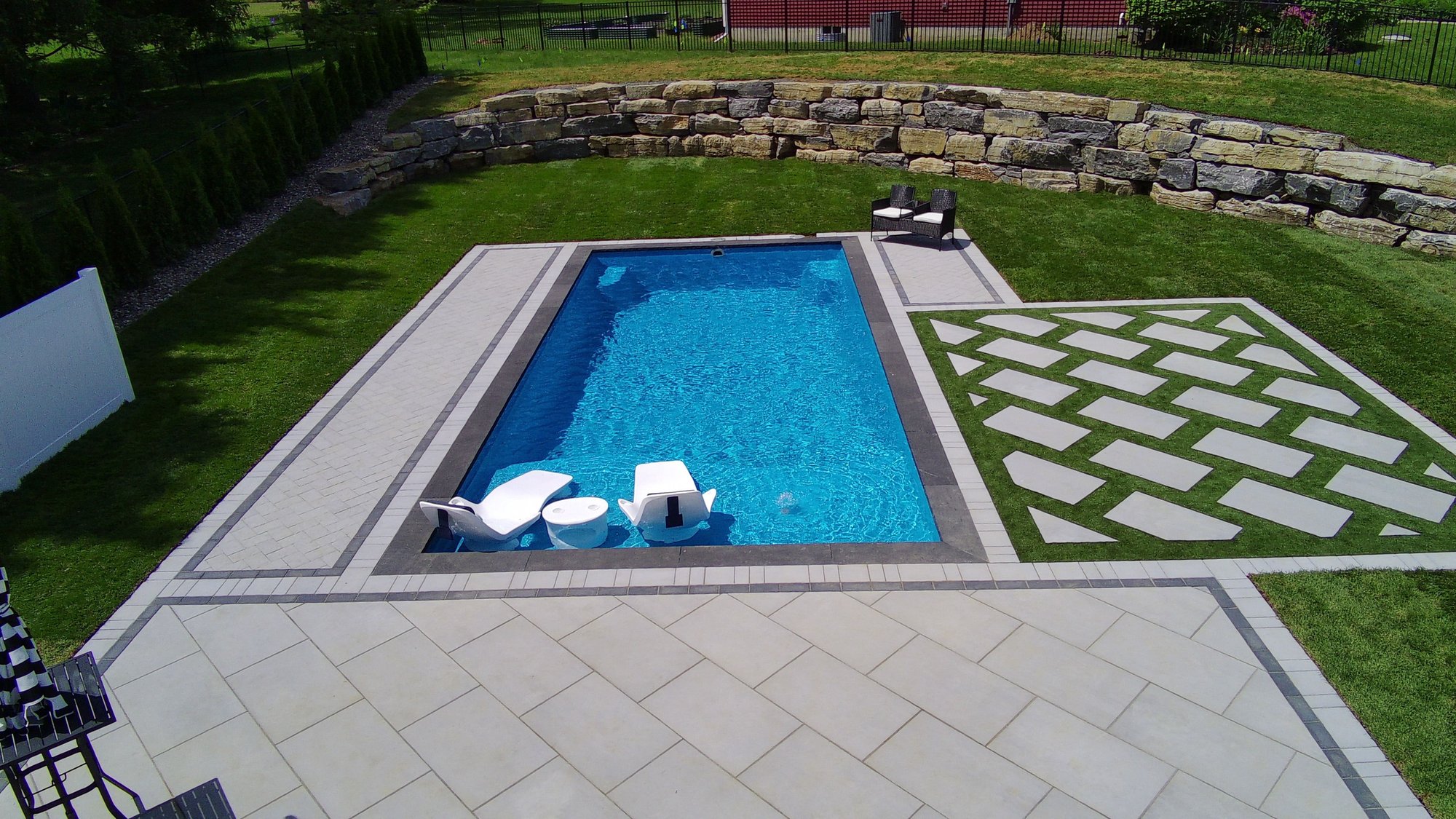 Rectangular fiberglass pool with tanning ledge and geometric pavers in Clifton Park, NY installation