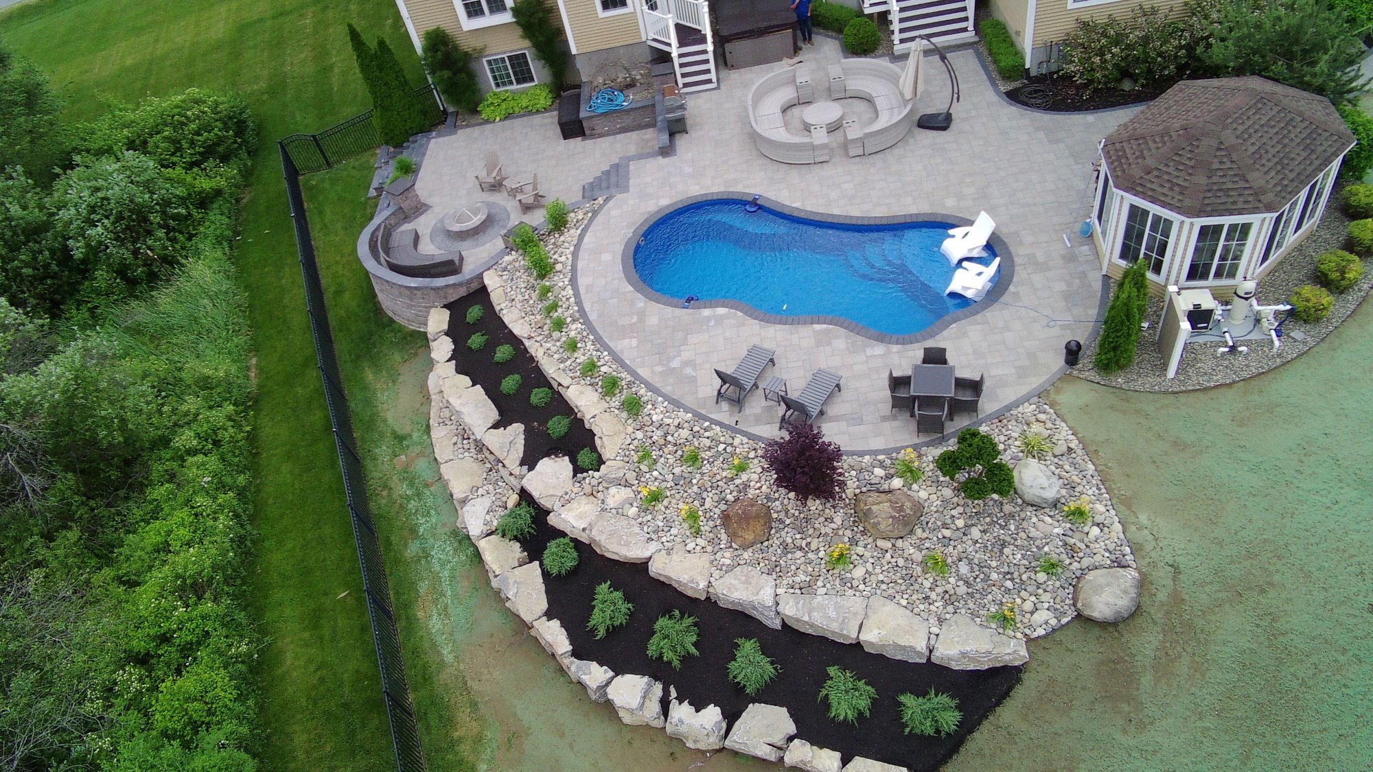 Curved fiberglass pool with built-in seating, paver patio, and landscape design in Saratoga Springs, NY
