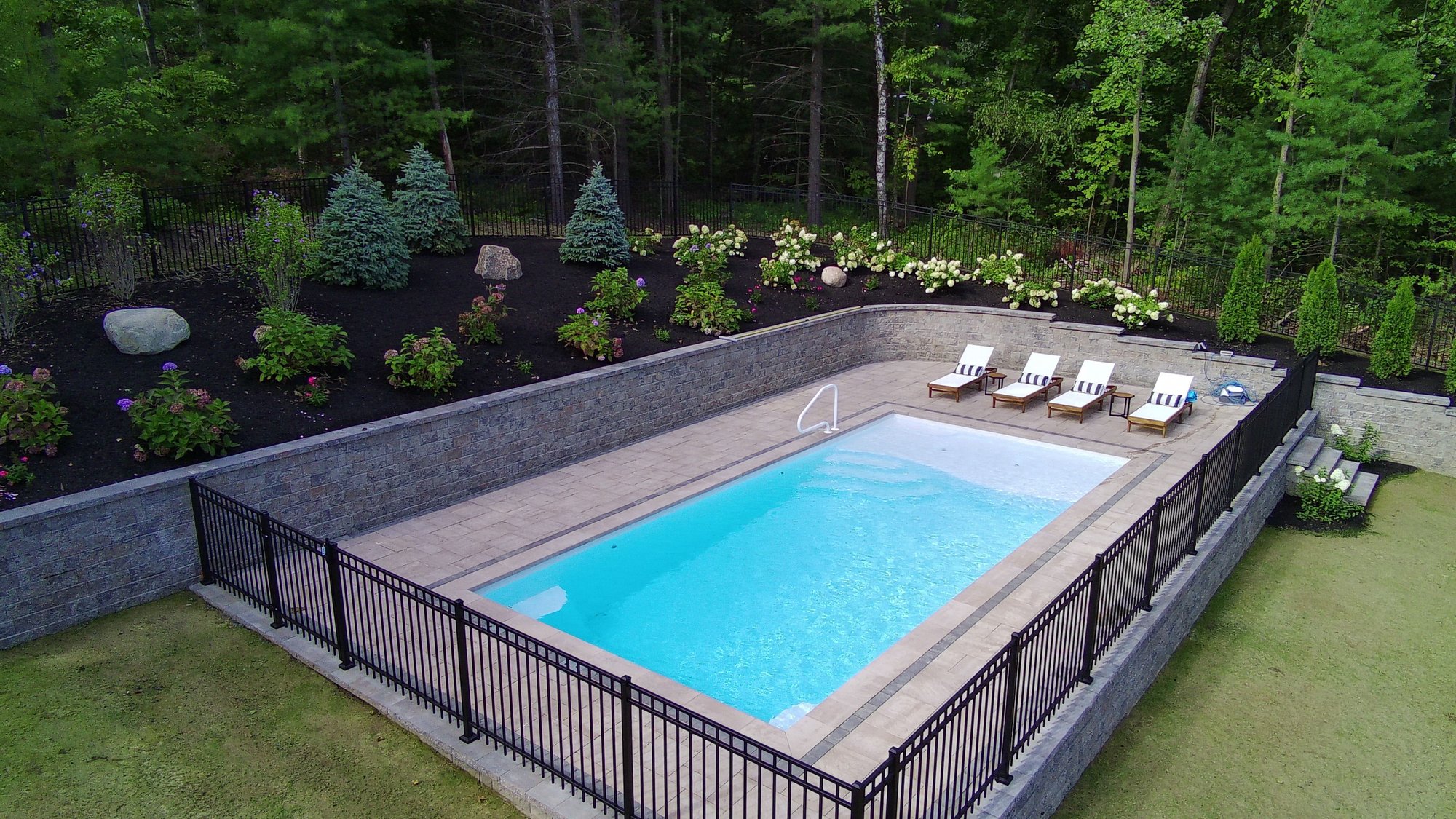 Modern rectangular fiberglass pool installation with raised landscaping and lounge chairs in Albany, NY backyard