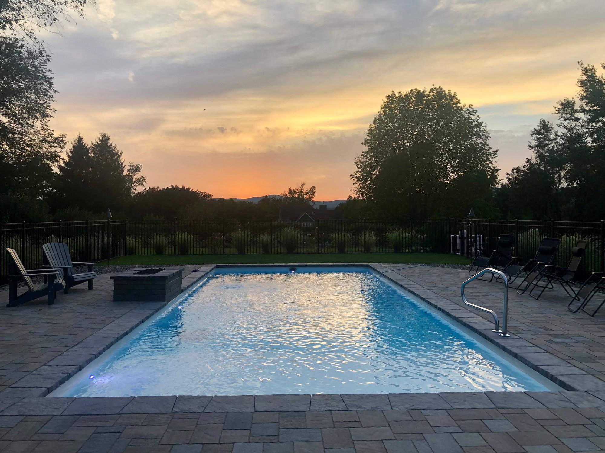Stylish inground fiberglass pool surrounded by stone retaining wall and green lawn in Troy NY