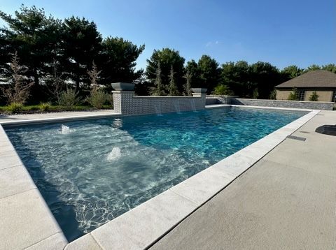 Modern fiberglass pool with a shallow tanning ledge and water features, installed by River Pools in Lenexa, Kansas.