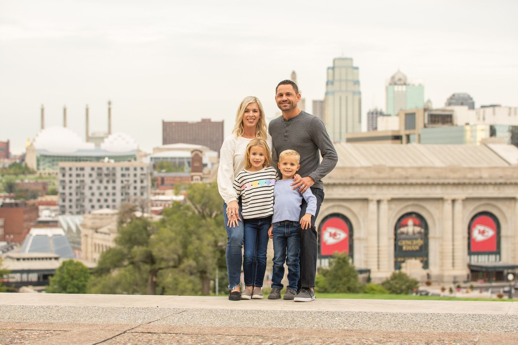 Jeff and Angela, owners of River Pools Kansas City, with their family in front of Union Station and the Kansas City skyline, proudly serving the KC metro with expert fiberglass pool installation.