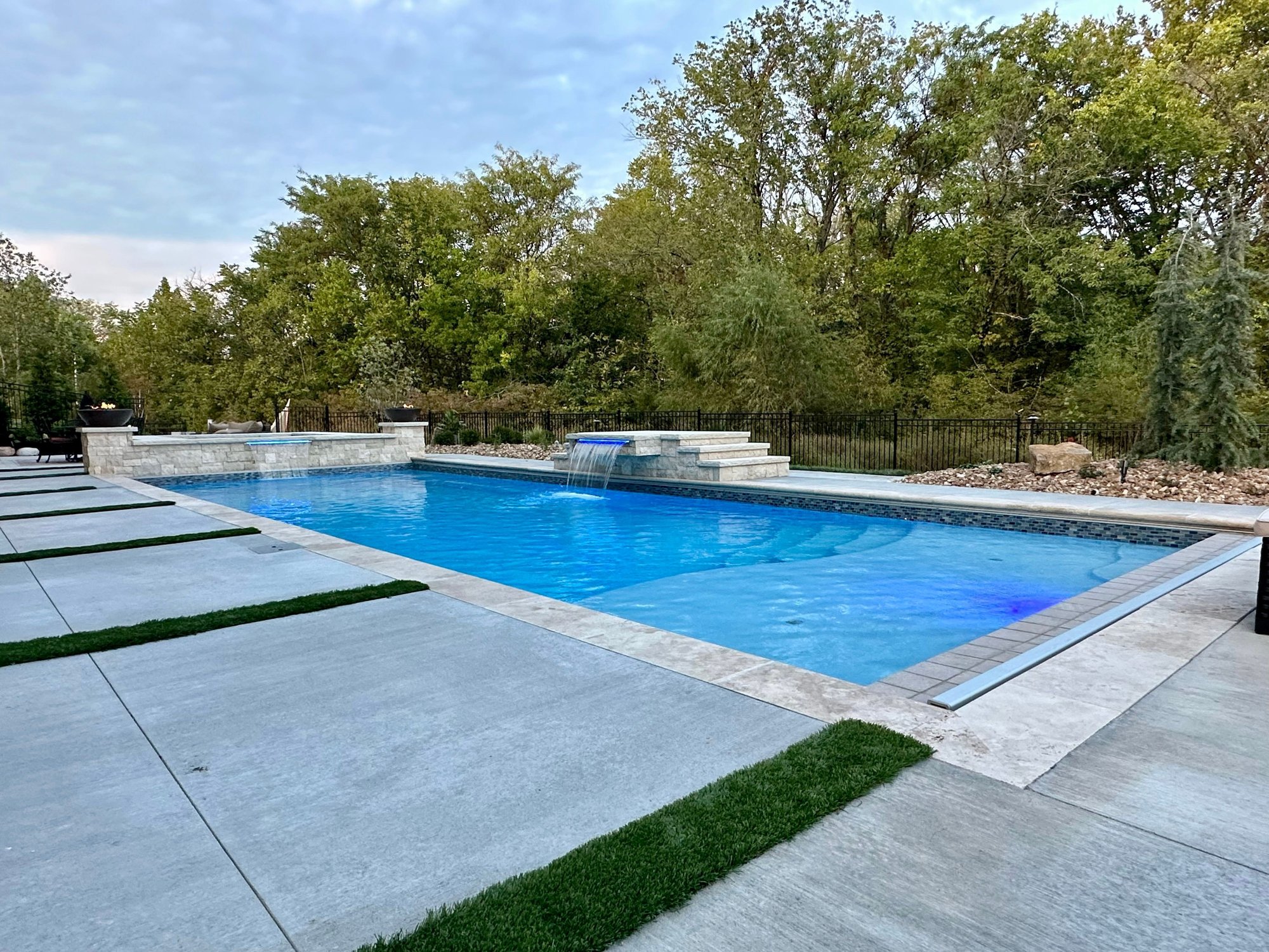 Spacious fiberglass pool with elevated water feature and modern landscaping in a Kansas City backyard.