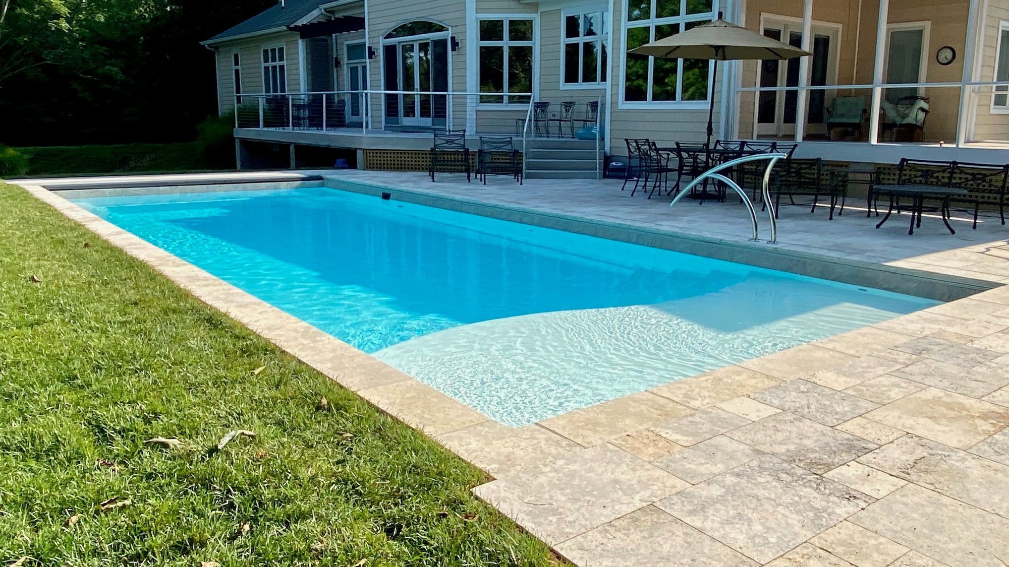 Fiberglass inground pool installation in Bella Vista, AR, with travertine patio, tanning ledge, and modern stainless steel water feature.