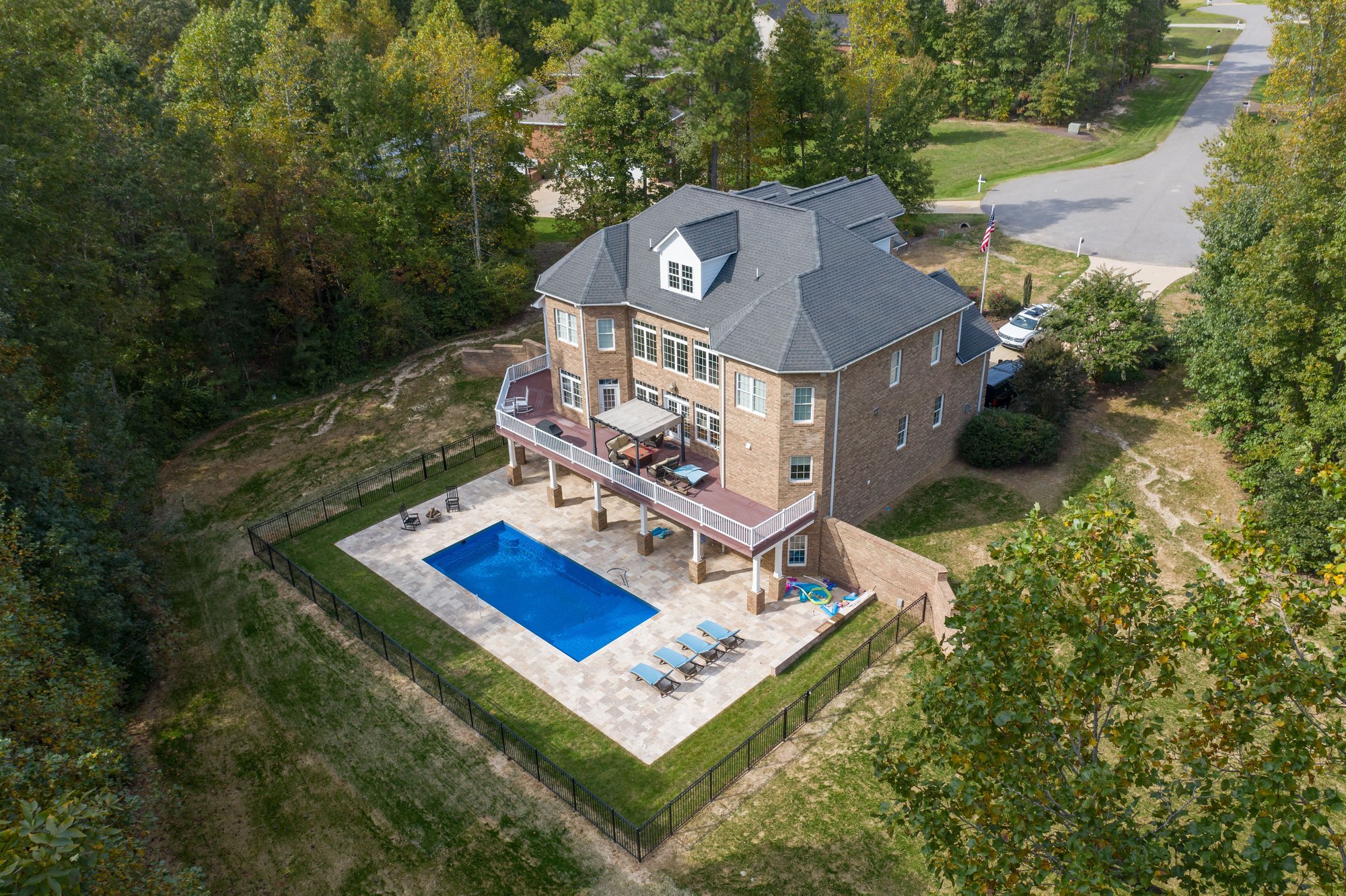 Fiberglass inground pool installation in Ozark, MO, with elevated deck, travertine patio, and fenced hillside backyard.