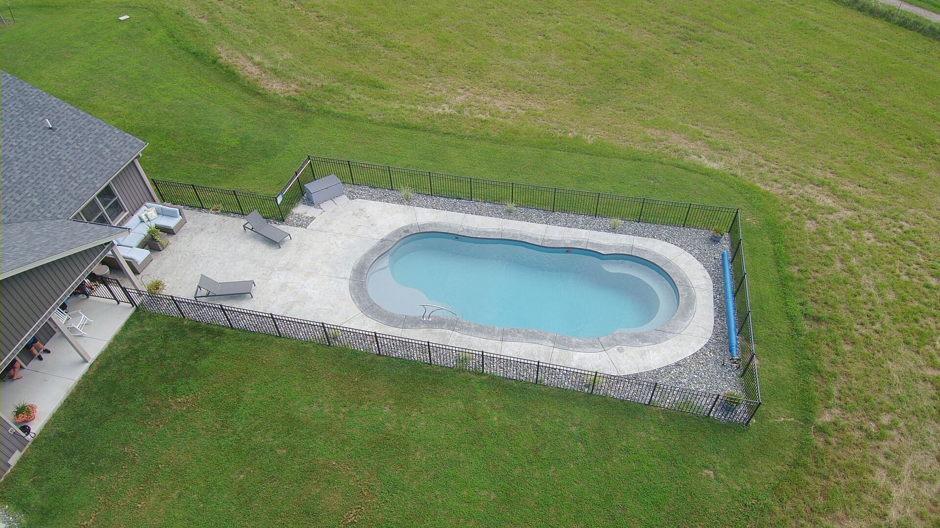 Freeform fiberglass pool installation in Fayetteville, AR with concrete deck and fence
