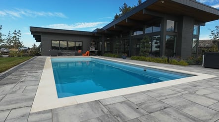 Modern fiberglass pool installed by River Pools Red Wing with custom paver patio and sleek architectural home in the background.