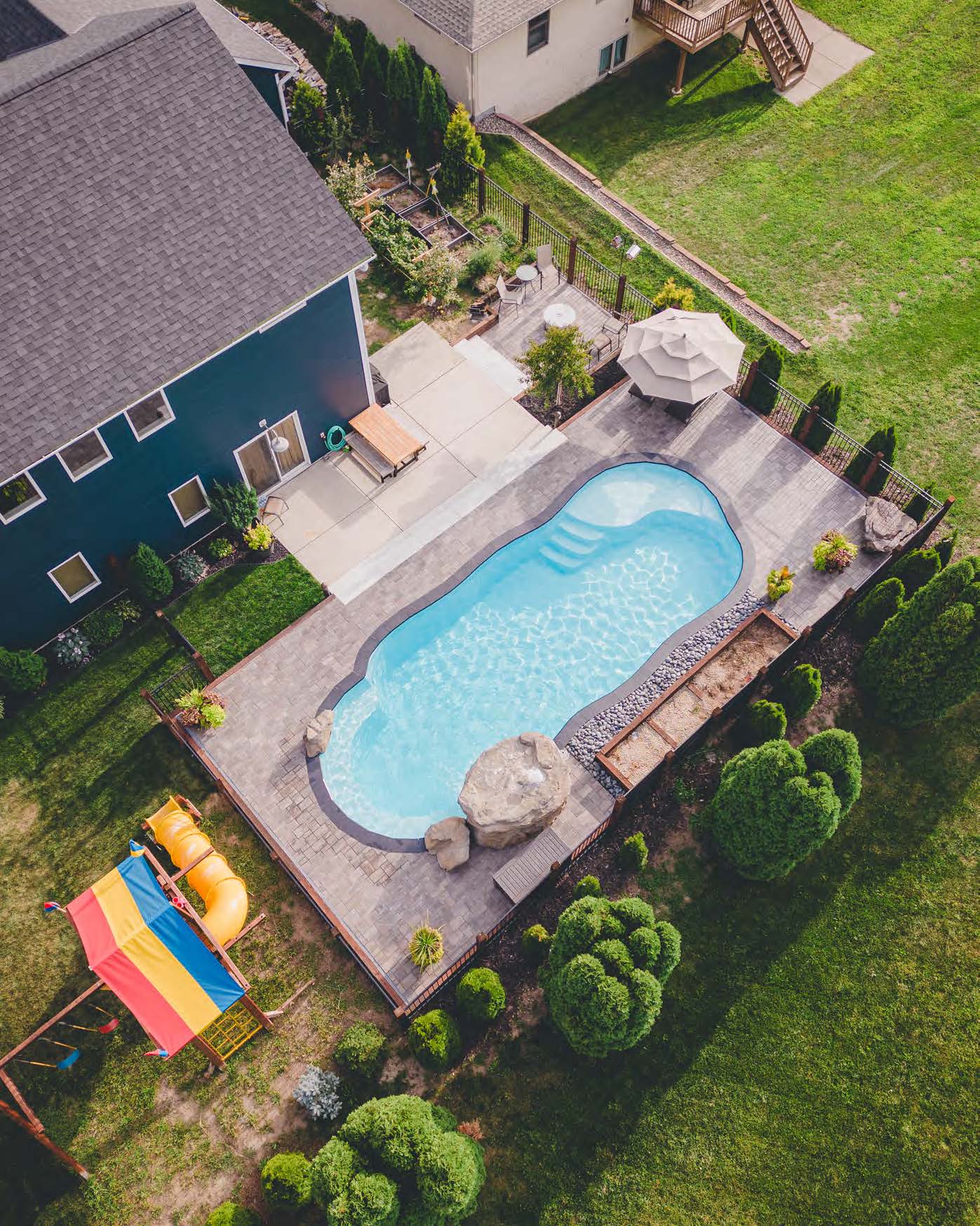 Freeform fiberglass pool with rock water feature and paver patio in a family-friendly backyard near Red Wing, Minnesota, built by River Pools Red Wing..