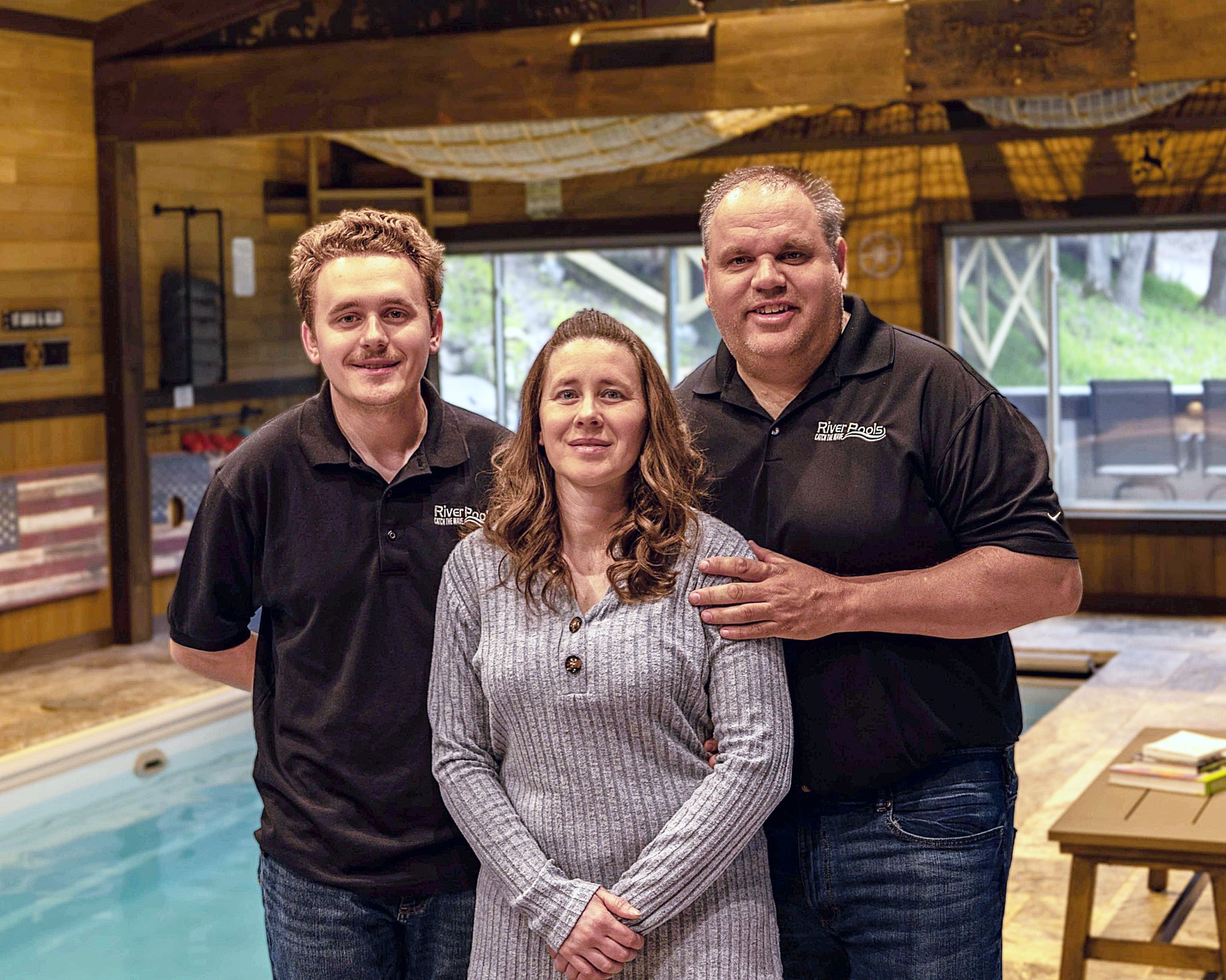 Andrew, Anji, and their son Drew of River Pools of Red Wing standing together in front of an indoor fiberglass pool, representing their family-owned pool installation business.