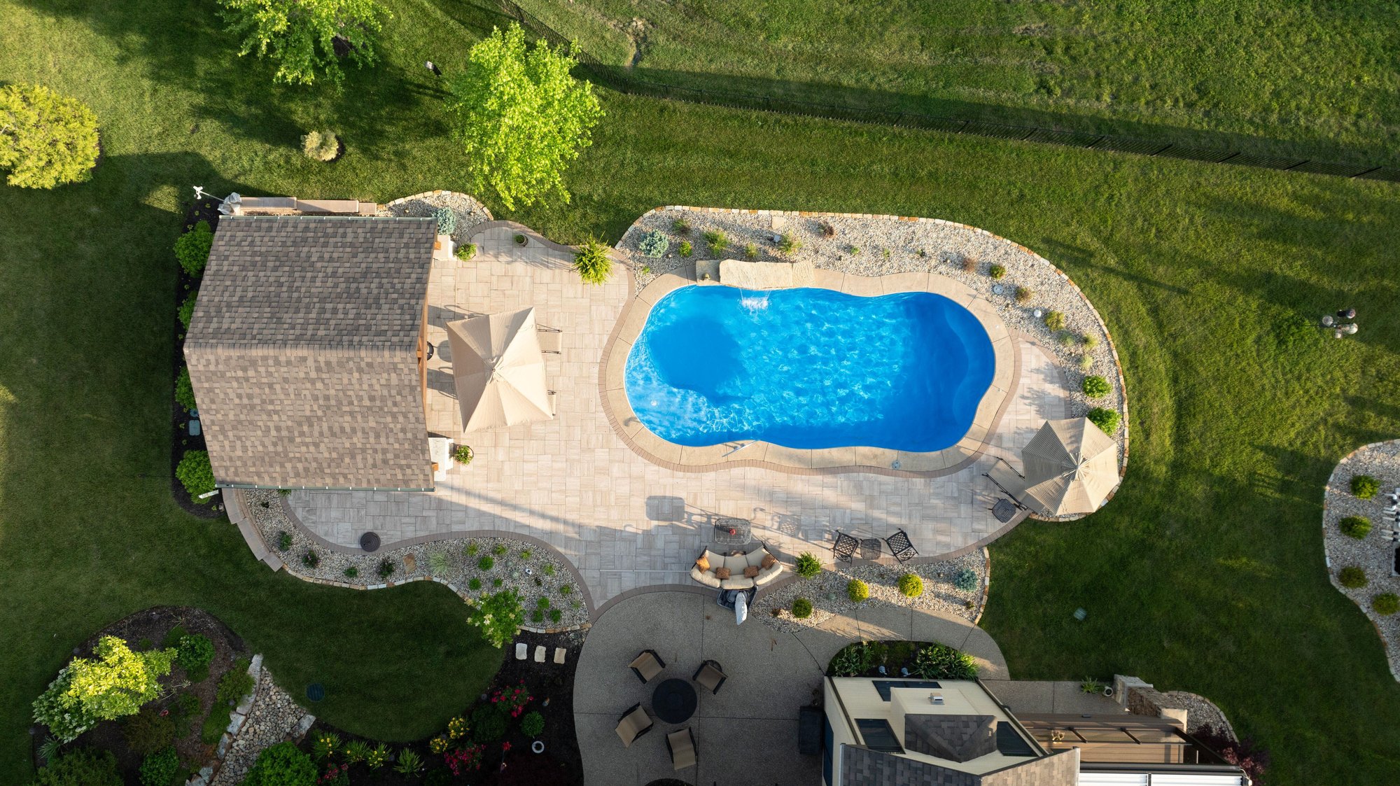 Aerial view of a fiberglass pool installation in St. Louis, MO featuring custom paver patio, pool house, and landscaping by River Pools St. Louis