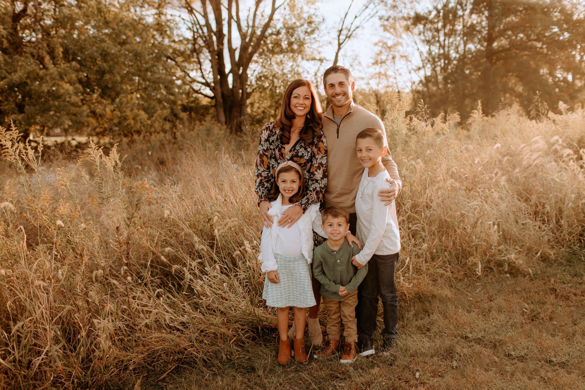 Joe and Kristin Giger with their three children, owners of River Pools St. Louis, standing together in a sunlit field.
