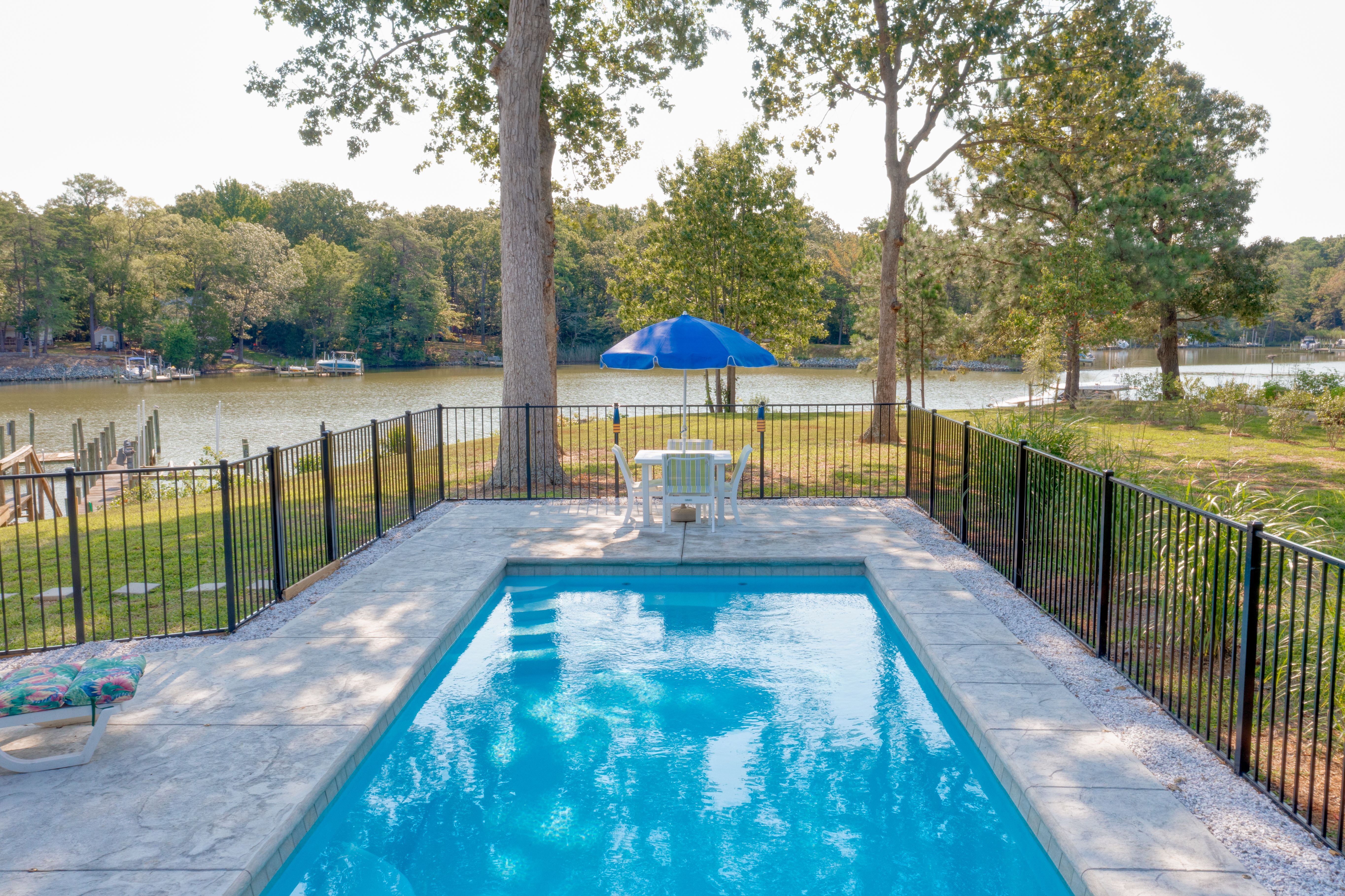 Fiberglass plunge pool on a Northern Neck riverfront property with black fencing and umbrella seating overlooking the water.