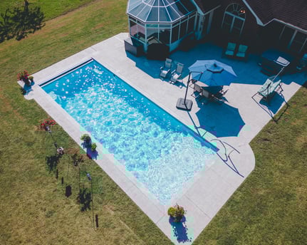 Aerial view of a fiberglass pool installed by River Pools Savannah in an open backyard with patio furniture, umbrellas, and colorful landscaping.