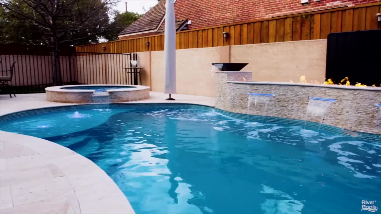 I Series fiberglass pool with cascading water features and a modern fire bowl accent wall.