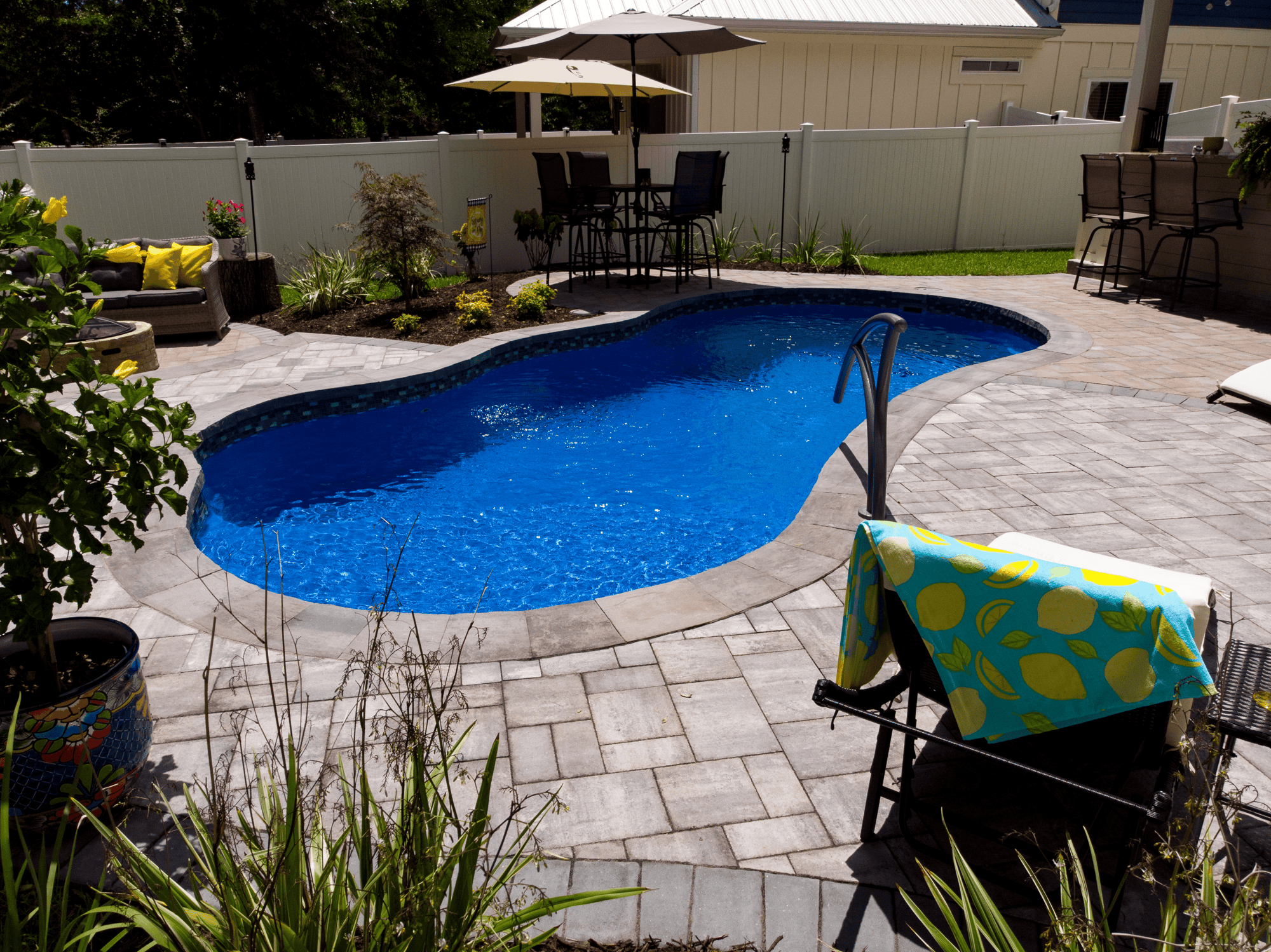 Backyard entertainment setup with I25 Series fiberglass pool, pavers, and lounge seating.