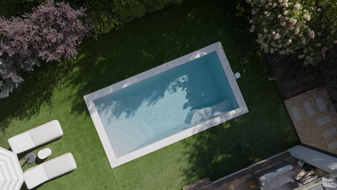 Drone view of River Pools R20 fiberglass pool with clean lines, entry steps, and artificial turf landscaping.