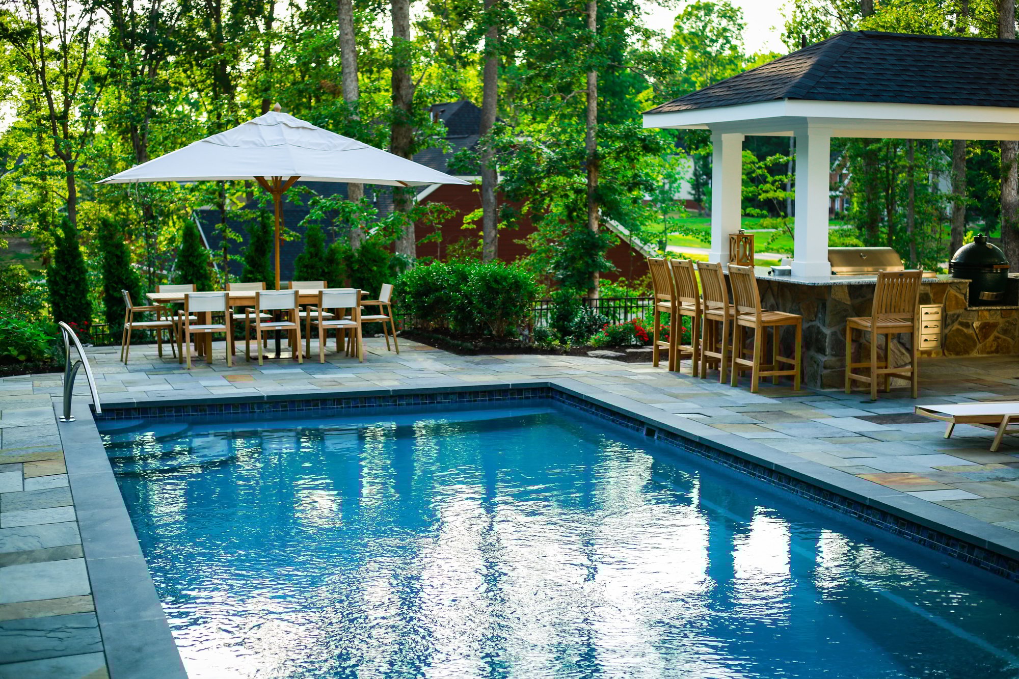 River Pools T40 fiberglass pool featuring a nearby dining set and a covered bar structure on a stone patio.