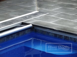 Automatic pool cover track, lid system, and leading edge bar on River Pools fiberglass pool. Pool coping is bluestone. Pool color- Maya Blue Tile- Aztec Cobalt.