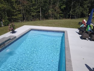 R32 pool in Caribbean with paver coping and brushed concrete decking featuring a cascade water feature