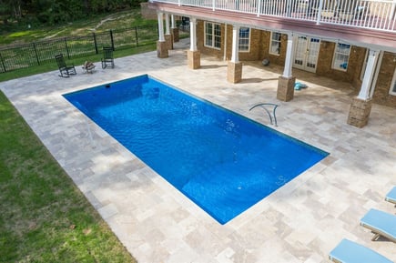 Rectangular fiberglass inground pool with large paver patio and covered outdoor living space.