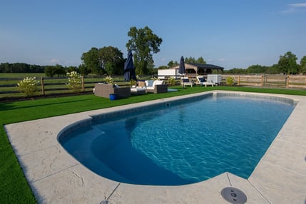 Rectangular fiberglass inground pool with curved entry steps and concrete patio in open backyard setting.