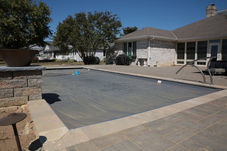 Fiberglass inground pool fully covered with an automatic safety cover, set in a spacious backyard with paver decking and landscaped surroundings.
