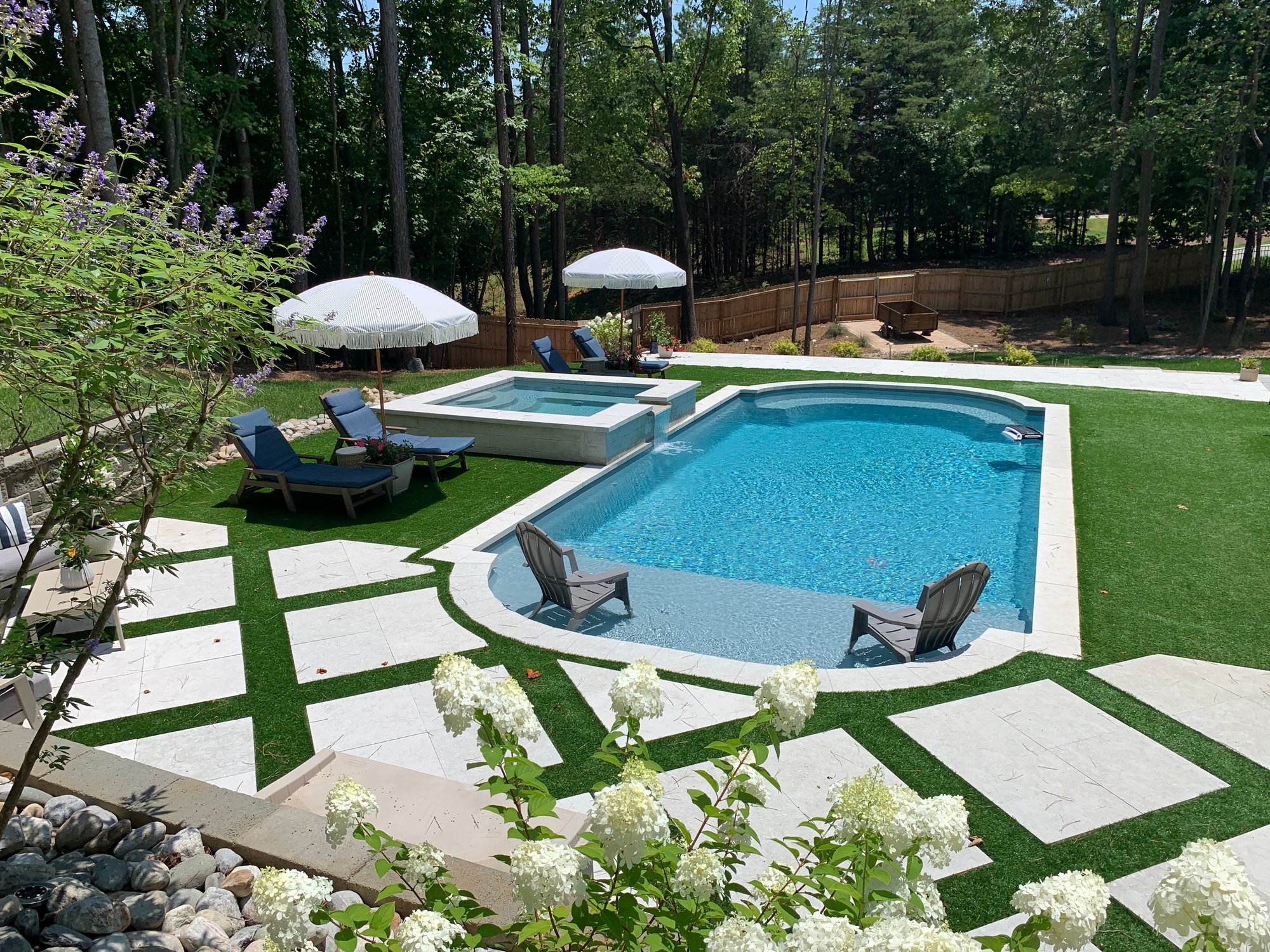 River Pools inground fiberglass pool with an added spa surrounded by artificial turf and wooded background. 