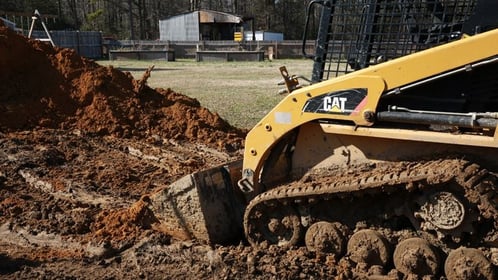 messy yard and dirt pile with a skid loader during fiberglass pool installation