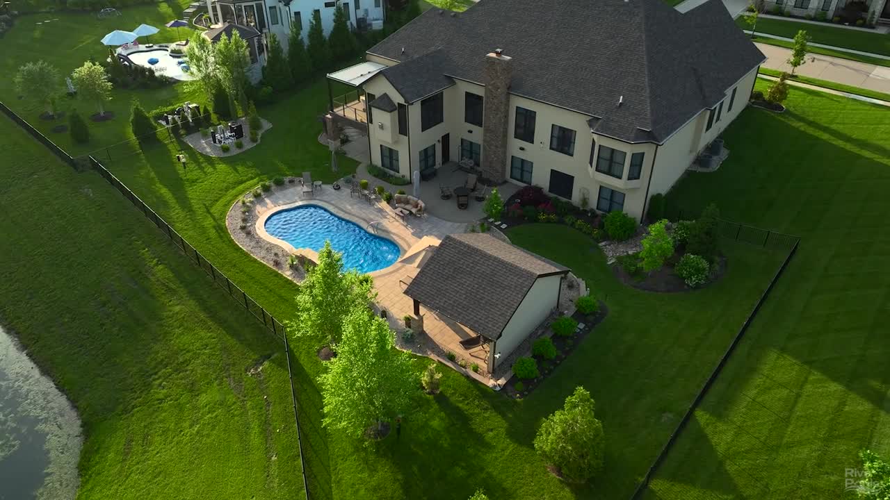 Aerial view of River Pools C35 fiberglass pool in California, featuring a curved design, white concrete deck, and paver patio set in a well-manicured backyard.