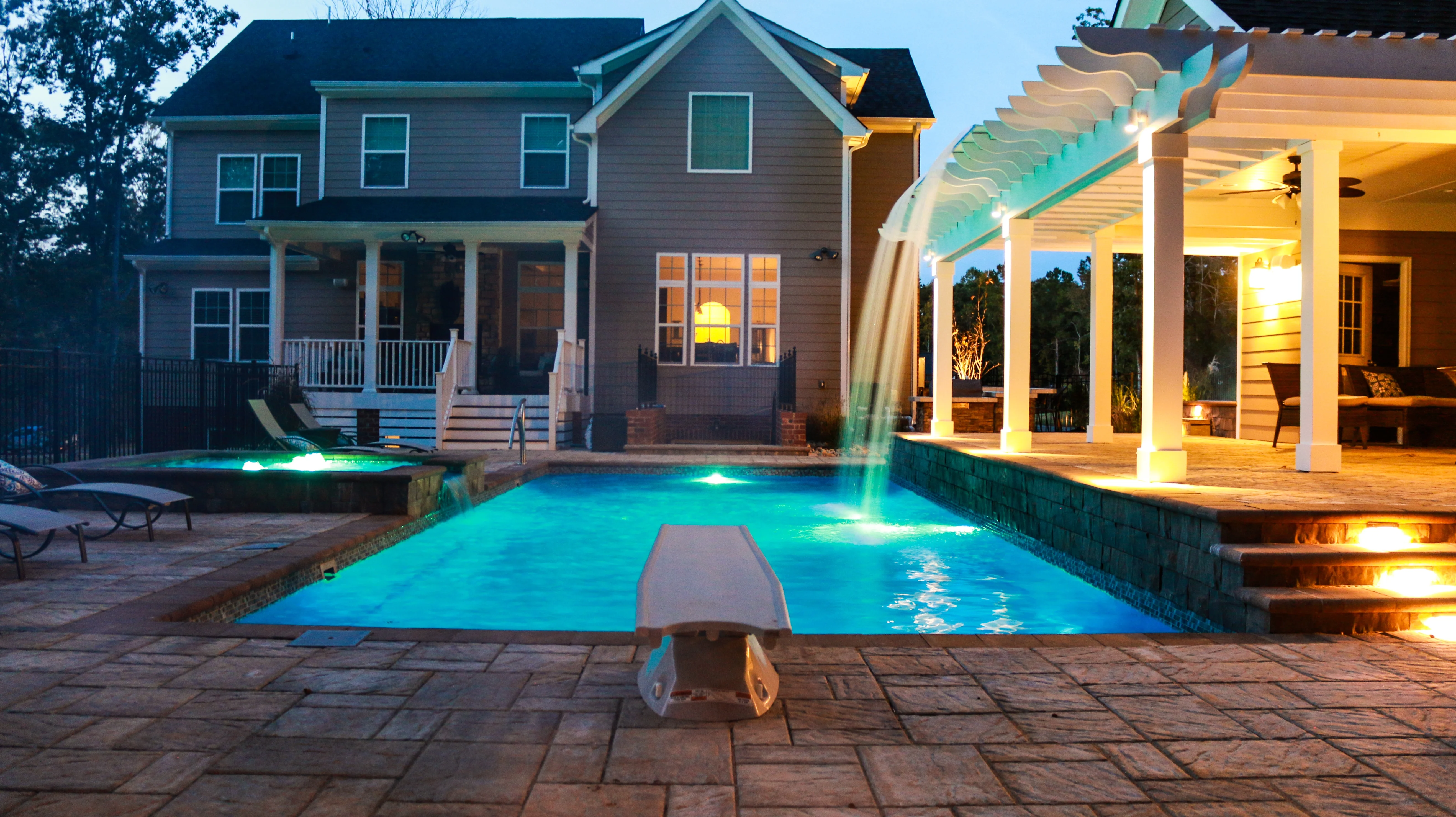 Nighttime shot of inground fiberglass pool with lights.