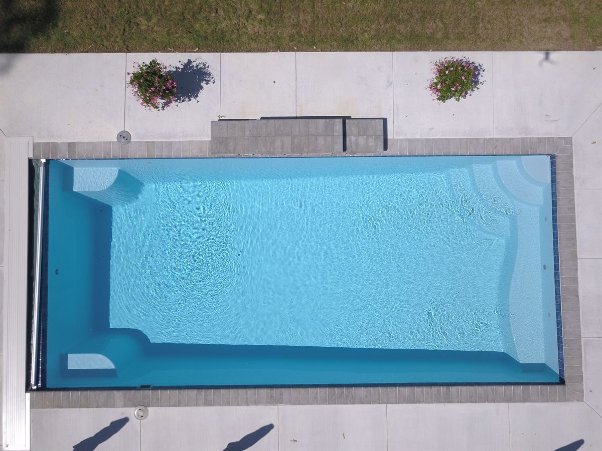 R32 pool in Caribbean with paver coping and brushed concrete decking featuring a cascade water feature