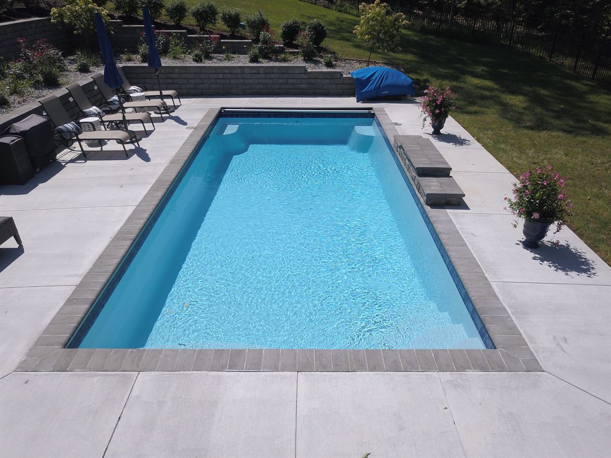 R32 pool in Caribbean with paver coping and brushed concrete decking featuring a cascade water feature