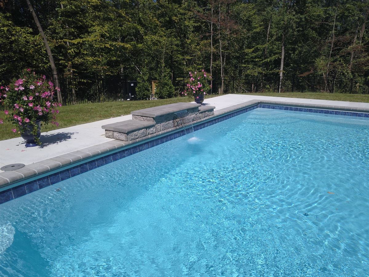 R32 pool in Caribbean with paver coping and brushed concrete decking featuring a cascade water feature