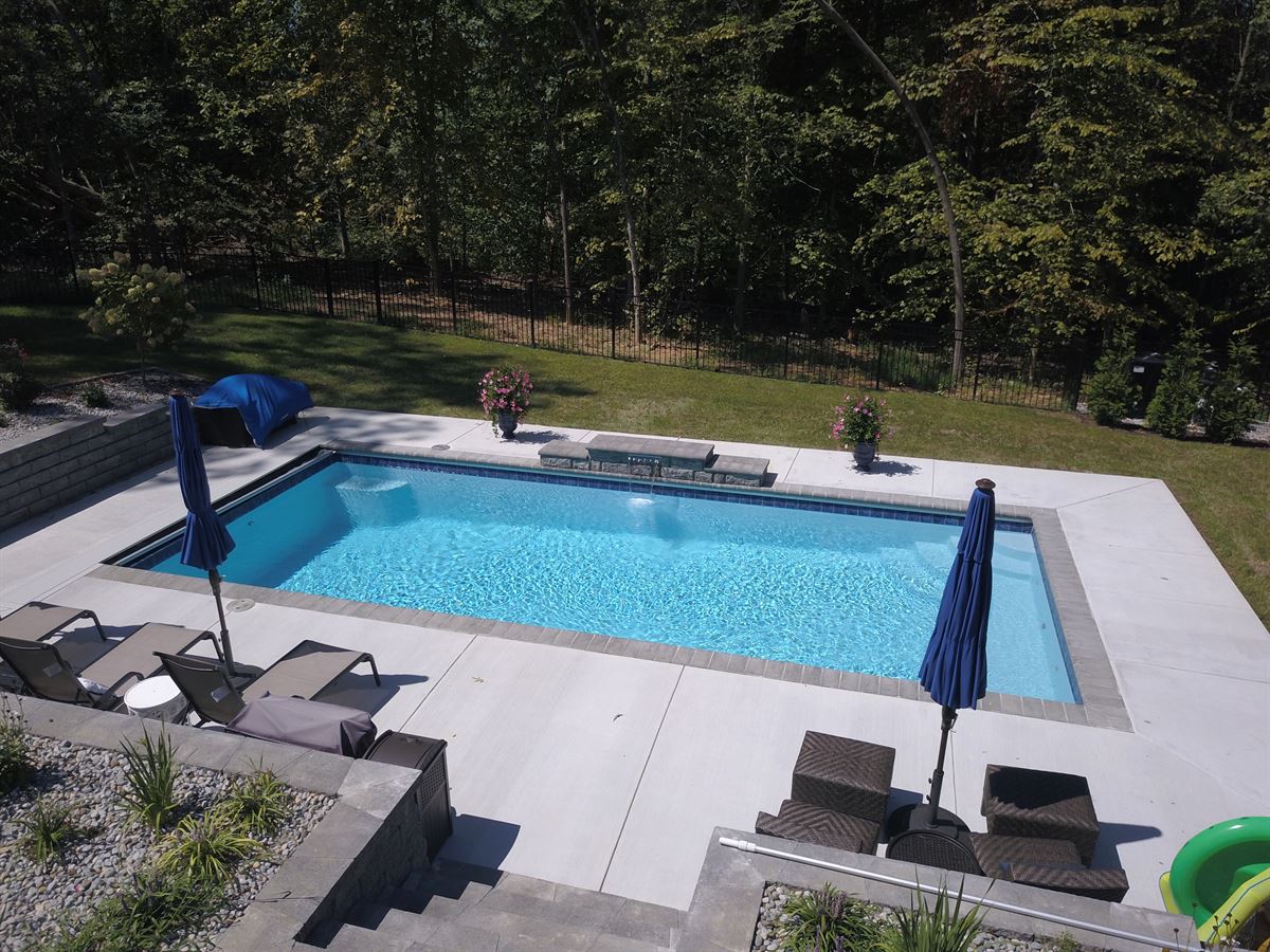 R32 pool in Caribbean with paver coping and brushed concrete decking featuring a cascade water feature