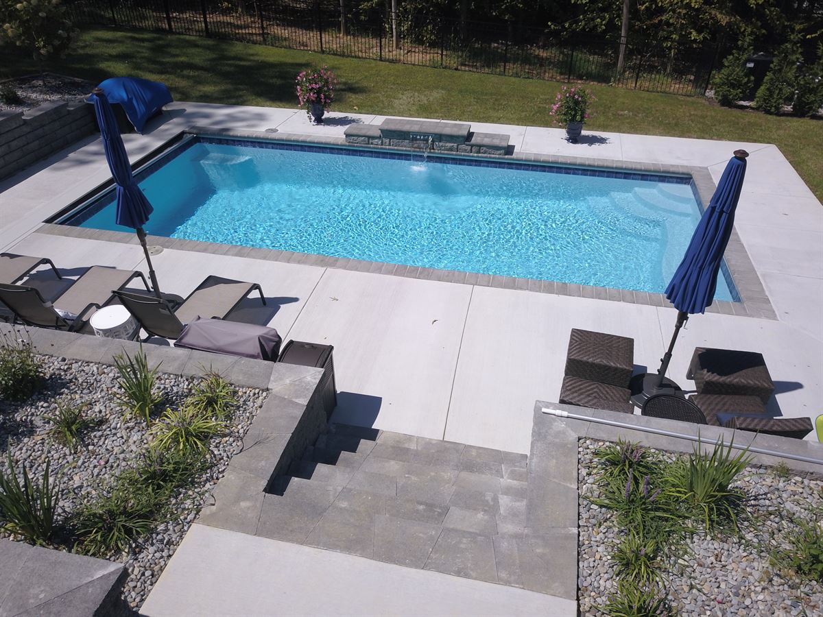 R32 pool in Caribbean with paver coping and brushed concrete decking featuring a cascade water feature