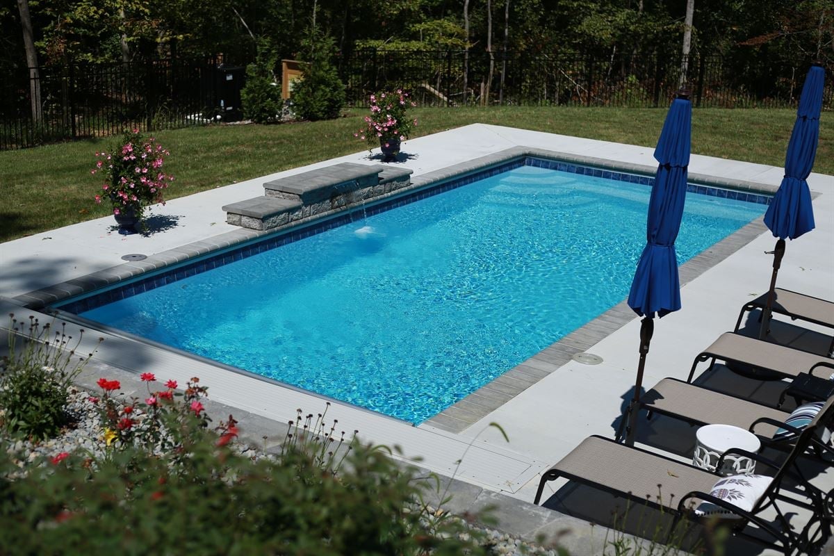 R32 pool in Caribbean with paver coping and brushed concrete decking featuring a cascade water feature