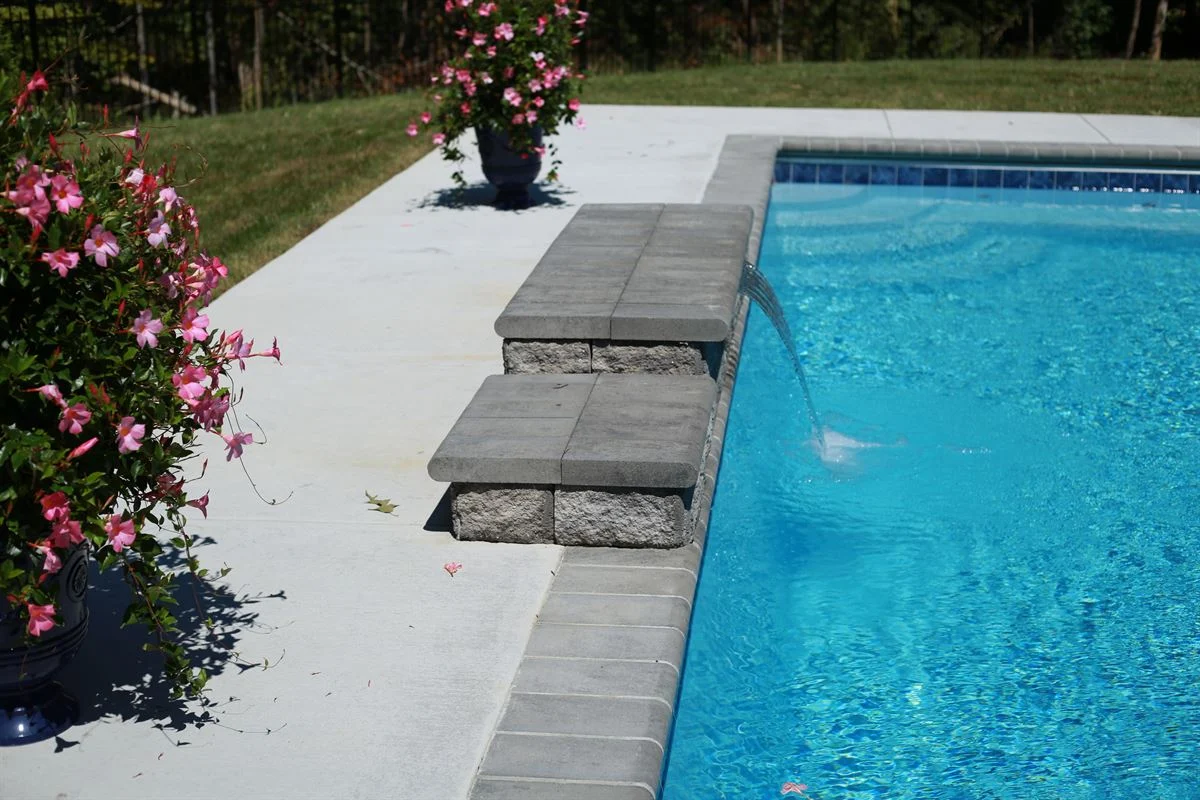 R32 pool in Caribbean with paver coping and brushed concrete decking featuring a cascade water feature