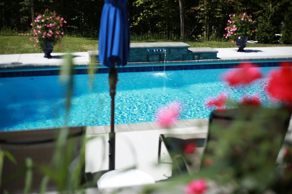 R32 pool in Caribbean with paver coping and brushed concrete decking featuring a cascade water feature